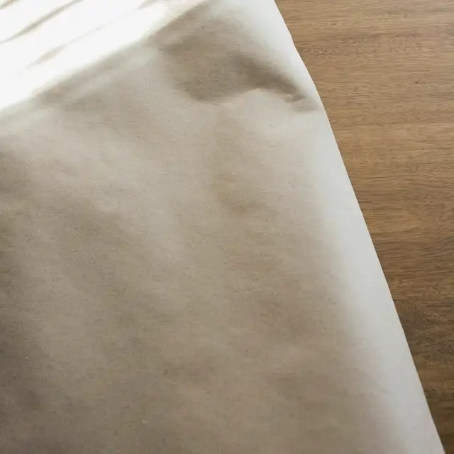 Sade bir masada katlanmış açık renk bir bebek battaniyesi ve üzerinde kapalı duran boş bir sağlık takip defteri; yumuşak yan ışık, görünen yüz ya da okunabilir yazı yok.