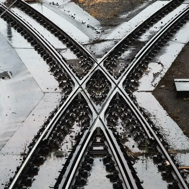 Islak zeminde birbirini kesen iki tren rayı, tam ortada belirgin bir X oluşturuyor.