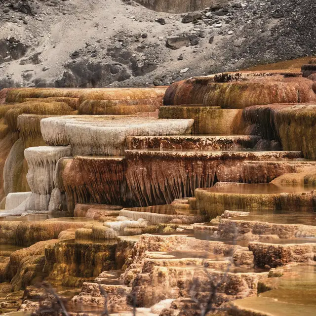 Travertenin teras basamakları; yüzyıllar boyunca katman katman birikmiş mineral kademeler, sıcak oker ve krem tonlarında.