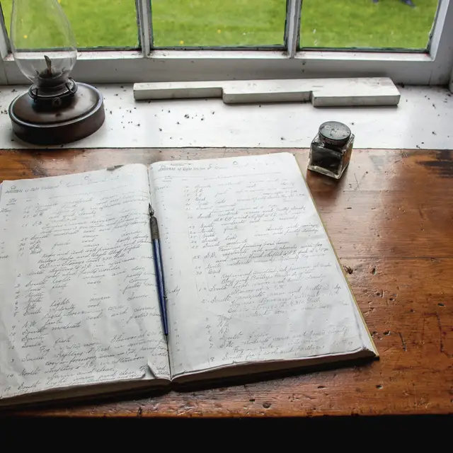 Pencere kenarında açık duran kalın bir defter; sayfalarda alt alta el yazısı satırlar var ama yazılar okunmuyor, üstünde bir dolmakalem duruyor.