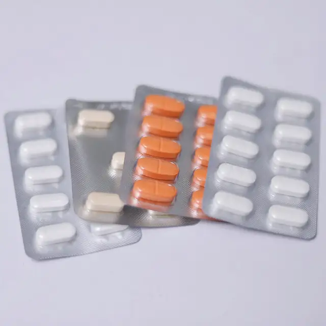Açık gri zeminde yelpaze gibi açılmış beş blister; içlerindeki tabletler beyaz, turuncu ve krem renkli, üzerlerinde okunabilir yazı yok.